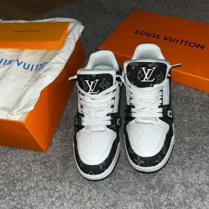 Louis Vuitton trainers  - Louis Vuitton sneakers i svart och vitt med klassiskt LV-monogram och logga på tungan och hälen. Skorna har snörning, platt sula och rund tå. Materialet är en mix av skinn och textil med monogramdetaljer. Snygg kontrast mellan svart och vit, perfekt för dig som gillar lyxiga streetwear-vibes.