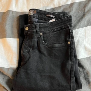 Svarta slim fit jeans från H&M - Svarta jeans från H&M med slim fit-passform. Klassisk femficksmodell med silverfärgade nitar och knapp. Jeansen har en enkel, stilren look och är tillverkade i stretchig denim för extra komfort.