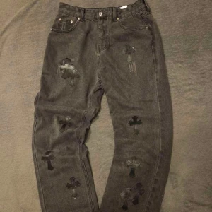 Chrome Hearts svarta jeans - Unika svarta jeans från Chrome Hearts med flera svarta läderkors som är fastsydda över hela byxorna. Klassisk femficksmodell i 100% bomull med raka ben och snygga detaljer. Perfekt för dig som vill sticka ut med en edgy streetwear-look.