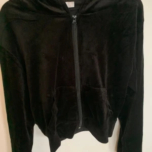 Svart velour hoodie och byxor - Mysig svart hoodie i mjuk velour från LUV. Tröjan har huva, dragkedja framtill och två fickor. Perfekt för chill dagar eller när du vill ha en skön och stilren look. Långärmad och med klassisk passform.