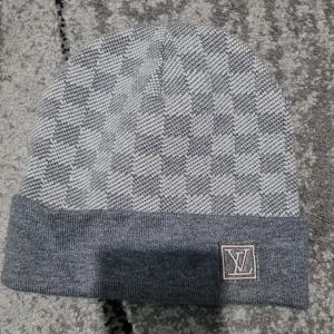 Grå rutig L&V mössa - Snygg grå mössa från L&V med klassiskt rutigt mönster och vikt kant. L&V-logga framtill i broderad patch. Perfekt accessoar för att hålla stilen kallare dagar. Mjuk och skön känsla, passar till det mesta.