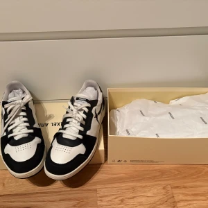 Svarta och vita sneakers från Axel Arigato - Snygga sneakers från Axel Arigato i svart och vitt med kontrasterande paneler och klassisk snörning. Skorna har rund tå, platt sula med logotyp och är tillverkade i skinn och mocka. Perfekta för dig som gillar stilrena och trendiga sneakers.