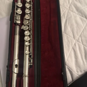 Yamaha tvärflöjt med fodral - Yamaha tvärflöjt i originalfodral med röd sammet. Flöjten är i gott skick med endast mindre tecken på användning. Perfekt för nybörjare och studenter. Fodralet är robust och skyddar instrumentet väl.