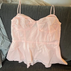 Ljusrosa korsett-topp med volang - Supersöt ljusrosa korsett-topp med tunna axelband och volang nedtill. Toppen har dragkedja i sidan, materialet är lätt och känns som bomull, perfekt för sommarens alla tillfällen.💕💕