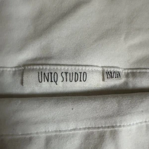 Vit offshoulder topp från UNIQ STUDIO - Säljer en vit offshoulder topp från UNIQ STUDIO i mjuk bomull. Toppen är ärmlös med bred krage som ligger snyggt över axlarna. Perfekt för dig som gillar minimalistisk och clean stil. Passformen är normal och materialet är skönt mot huden.