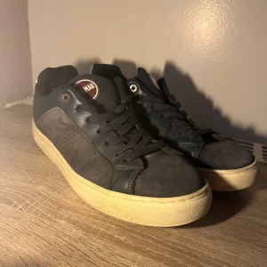 Mörkblå sneakers från Colmar, strl 43 - Snygga mörkblå sneakers från Colmar i storlek 43. Skorna har ovandel i mocka och skinn, vita detaljer baktill och vit platt sula. Klassisk rund tå och snörning framtill. Perfekta för dig som gillar stilrena och sportiga skor.