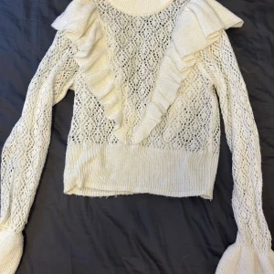 Vit stickad volangtröja H&M Divided  - Supersöt vit stickad tröja från H&M Divided i storlek S. Tröjan har ett genombrutet mönster, volanger framtill och vida ärmslut som ger en extra touch. Perfekt för dig som gillar romantiska detaljer och vill sticka ut lite extra.