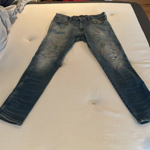 Replay Anbass blå slitna jeans - Säljer ett par Replay Anbass jeans i blå tvätt med slitna detaljer och snyggt distressed look. Jeansen har klassisk femficksdesign, smal passform och är tillverkade i mjukt jeanstyg. Perfekta för dig som gillar en trendig och avslappnad stil.