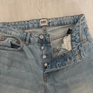 Ljusblå raka jeans från 157 - Ljusblå jeans från 157 med raka ben och klassisk femficksdesign. Jeansen har knäppning med flera silverfärgade knappar och subtila slitningar för en avslappnad look. Tillverkade i jeansmaterial med kontrastsömmar och normal passform.