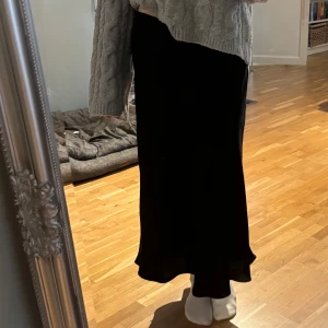 Svart långkjol från Zara i satin - Supersnygg svart långkjol från Zara i glansigt satinmaterial. Kjolen har en lätt utsvängd form och faller snyggt längs benen. Perfekt för dig som gillar en stilren och elegant look. Midjemodell och utan synliga detaljer för en clean vibe.