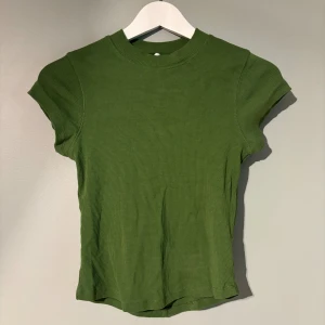 Grön ribbad topp från Topshop - Snygg grön ribbad topp från Topshop med korta ärmar och rund halsringning. Modellen är figurnära och har en enkel, stilren design som passar perfekt till jeans eller kjol. Materialet är mjukt och stretchigt för en bekväm känsla.