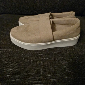 Beige loafers från VOX med platåsula - Snygga beige loafers från VOX med bred rem över foten och vit platåsula. Skorna har en rund tå och är gjorda i mockaliknande material som ger en soft känsla. Perfekta för dig som gillar stilrena och bekväma skor med lite extra höjd.