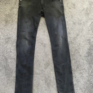 Replay Anbass svarta jeans slim fit - Svarta Replay Anbass jeans i slim fit med klassisk femficksdesign och snygga slitningar. Jeansen har normal midja och raka ben, tillverkade i stretchig bomullsdenim för skön passform. Perfekta för dig som gillar en stilren och modern look.