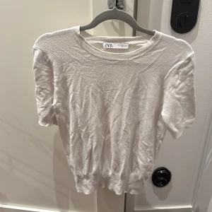 Vit kortärmad tröja från Zara - En stilren vit kortärmad tröja från Zara i mjukt material. Tröjan har rund halsringning och en enkel, klassisk design som passar perfekt till jeans eller kjol. Perfekt för vår och sommar när du vill ha en clean och fräsch look.