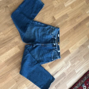 Blå jeans från Jack & Jones - Säljer ett par klassiska blå jeans från Jack & Jones med relaxed knappgylf och raka ben. Materialet är slitstarkt denim i bomull och färgen är snyggt tvättad blå. Perfekt för dig som gillar en chill och enkel stil. 