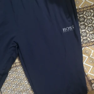 Mörkblå shorts från BOSS - Snygga mörkblå shorts från BOSS med diskret logga framtill och bakficka med dragkedja. De har elastisk midja och är perfekta för en clean och stilren look. Materialet känns lätt och passar bra till varmare dagar.
