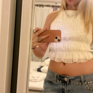 Topp  - Säljer en vit croppad linnetopp med omlott och knyt i ryggen. Toppen är ärmlös och har volangkant nedtill samt ribbad struktur. Perfekt för sommarens varma dagar och har en öppen rygg för extra chill vibe.