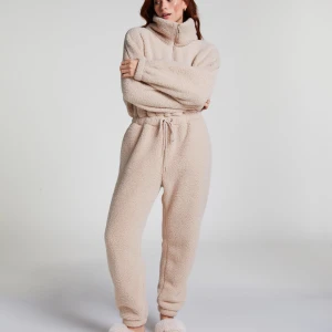 Beige teddy byxdress med snörning - Supermjuk och fluffig beige byxdress i teddy-material med dragsko i midjan och half zip framtill. Perfekt för chill dagar hemma. Tillverkad i 100% polyester och har en relaxed fit med långa ben och ärmar.Beige teddy byxdress med snörning