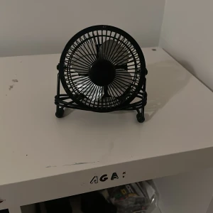 USB Mini Fläkt - Kompakt USB-driven bordsfläkt i svart metall. Perfekt för skrivbordet eller resan. Fläkten är i gott skick med mindre tecken på användning, inga synliga defekter. Lång USB-kabel medföljer för flexibel placering. Tystgående och energieffektiv.