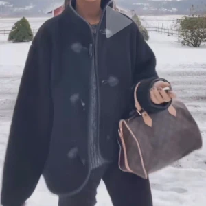 Svart teddyjacka med knappar - Mysig svart teddyjacka med oversized passform och snygga detaljer i form av stora knappar och kantband i skinnimitation. Jackan har hög krage och lång ärm, perfekt för kyliga dagar. Enkel att styla till olika outfits och riktigt trendig.