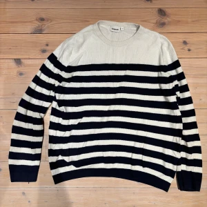 Randig stickad tröja från Kappahl - Snygg stickad tröja från Kappahl i storlek L. Tröjan har breda marinblå och vita ränder, rund hals och långa ärmar. Perfekt för dig som gillar klassisk stil med en modern twist. Materialet är mjukt och skönt, passar bra till jeans eller chinos.