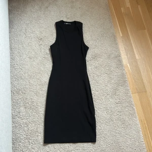 Svart ärmlös midiklänning - En stilren svart ärmlös klänning med tight passform och rund halsringning. Klänningen är midilång och tillverkad i ett mjukt material som sitter snyggt på kroppen.