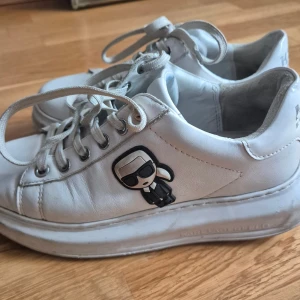 Vita sneakers med plattform - Snygga vita sneakers från Karl Lagerfeld med plattformssula och snörning. Skorna är i skinn och har en cool Karl Lagerfeld-figur på sidan samt logga baktill. Perfekt för dig som gillar statement-detaljer och vill ha en trendig look.