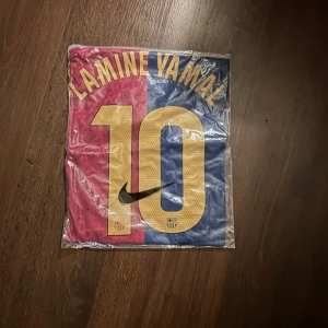 FC Barcelona Lamine Yamal tröja Nike M - Säljer en officiell FC Barcelona matchtröja med Lamine Yamal och nummer 10 på ryggen. Tröjan är kortärmad, tillverkad i lätt och ventilerande material. Färgerna är klassiskt röd och blå med gula detaljer, klubbmärke, Nike-logga och Spotify som sponsor framtill.