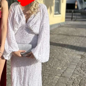 Vit långklänning med paljetter - Säljer en vit långklänning med glittriga paljetter och v-ringad front. Klänningen har ballongärmar, öppen rygg och dragkedja bak. Den är si storlek S, Jag som i vanlig fall har S passar den på, jag är cirka 167 och passar mig och även folk som är längre, den har ett släp bakom sig och den har tecken på användning nere vid släpet men är inget som sysn utifrån men ska föröska få bort de (kan skicka bild) 