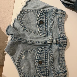 Blå jeansshorts från Pull&Bear - Säljer ett par blå jeansshorts från Pull&Bear i storlek 34. De har låg midja, råa och fransiga kanter, slitna detaljer och klassiska fickor både fram och bak. Liten ihop sydd slitning som visas på sista bilden. Säljer då de är för stora tyvärr.
