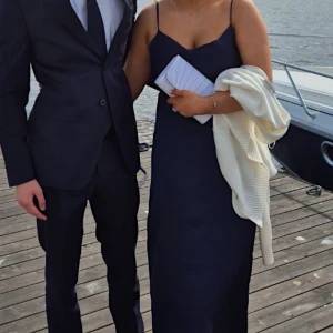 Marinblå långklänning i satin - Säljer en marinblå långklänning i satin med tunna axelband och djup öppen rygg. Klänningen har en elegant, figurnära passform och faller snyggt längs kroppen. Passar perfekt till bal eller festligare tillfällen! Skriv för fler bilder🙌🏼