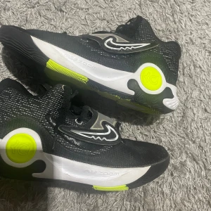 Nike KD Trey 5 sneakers svart/neon - Nike KD Trey 5 sneakers i svart med neon-gula och vita detaljer. Snyggt mönstrad mesh-överdel, coola KD-loggor och kontrasterande sula med Air Zoom-teknologi. Skorna har snörning och en unik design på tungan och yttersulan. Perfekt för dig som gillar basket och streetstyle.