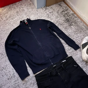Ralph lauren tröja  - Säljer denna marinblå Ralph Lauren full zip med den klassiska loggan på framsidan. Tröjan har långa armar, ståkrage och dragkedja framtill. Perfekt för laget-på-lager och enkel att matcha med ett par snygga jeans. 