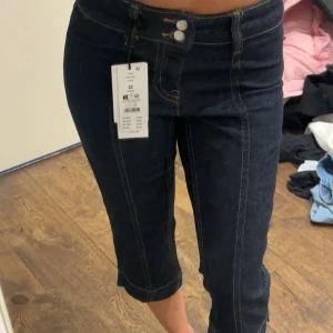 Mörkblå croppade jeansbyxor (capri) - Snygga mörkblå croppade jeansbyxor med kontrastsömmar och dubbla knappar i midjan. Modellen har raka ben och markerad söm framtill för en cool look. Perfekt för dig som gillar stilrena och trendiga jeans. Oanvända!