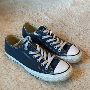 Converse All Star blå sneakers - Klassiska Converse All Star sneakers i marinblått tyg med vita gummisulor och tåhättor. Skorna har vita snören, silverfärgade öljetter och tydlig logga baktill. Perfekta för en avslappnad och cool stil. Storlek 37-38