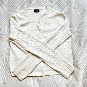 Vit kofta från Massimo Dutti 100% bomull  - Snygg vit kofta från Massimo Dutti i 100% bomull. Den har ett klassiskt kabelstickat mönster, rund halsringning och knappar framtill. 