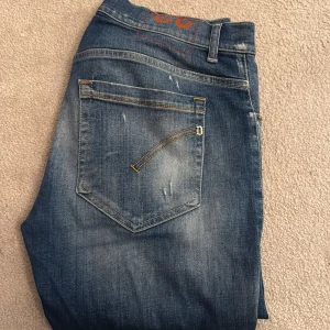 Blå skinny jeans från Dondup, stl 33 - Säljer ett par blå skinny jeans från Dondup i storlek 33. Jeansen har slitna detaljer och hål på benen för en cool, avslappnad look. Klassisk femficksmodell med snygga kontrastsömmar och lätt tvättad finish. Perfekta för dig som gillar streetstyle.