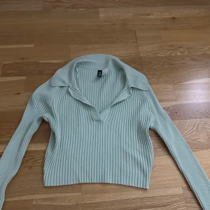 Ribbad mintgrön polotopp från H&M Divided - Säljer en snygg mintgrön polotopp från H&M Divided i storlek S. Toppen är ribbad, har lång ärm och en klassisk krage med v-ringad öppning framtill. Materialet är mjukt och stretchigt, perfekt för att ge en cool och fräsch look.