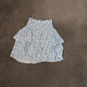 Blåvit blommig volangkjol - Supersöt kort kjol i blått och vitt med blommigt mönster och volangdetaljer. 