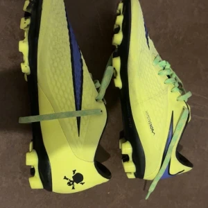 Nike Hypervenom fotbollsskor gul/blå - Nike Hypervenom fotbollsskor i neon-gult med blått swoosh och svarta detaljer. Passar för storlekerna 40-42