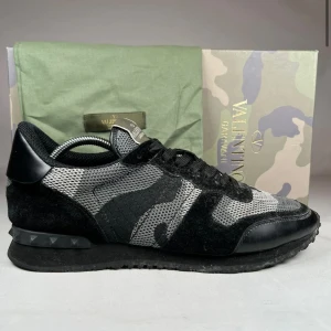Valentino Garavani Rockrunner sneakers - Snygga Valentino Garavani Rockrunner sneakers i svart och grått med camouflage-mönster. Ovandel i mesh och mocka, svarta skosnören och coola nitar på hälen. Perfekta för dig som vill sticka ut med exklusiva och trendiga sneakers.