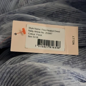 Blommig plisserad kortklänning Nelly - Säljer en ljusblå plisserad kortklänning från Nelly med blommigt mönster. Klänningen har omlott-v-ringning, långa ärmar och volangdetaljer framtill. Perfekt för dig som gillar romantisk och flowy stil. Materialet är lätt och ger en snygg siluett.