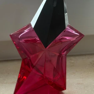 Mugler Stjärnformad parfymflaska i rosa - Cool parfym i unik stjärnformad flaska med rosa och svart design. Perfekt för dig som vill sticka ut och ge din samling en färgklick. Märket är Mugler, populärt bland unga vuxna. Volym och ingredienser syns ej på bilden.