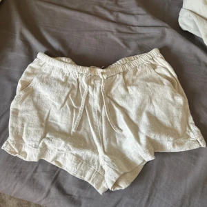 Beiga linneshorts med snörning - Snygga och luftiga beiga shorts i linne med elastisk midja och snörning framtill. Perfekta för varma dagar och har praktiska fickor på sidorna. Avslappnad passform och mjukt material som känns skönt mot huden.