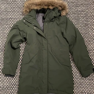 Grön parkas från Didriksons - Säljer en mörkgrön parkas från Didriksons i st 160. Huvan har en löstagbar reflekterande fuskpälskant. Den vattentäta jackan har quiltat grått innerfoder, dragkedja och knappar framtill samt stora fickor. Mycket bra skick!