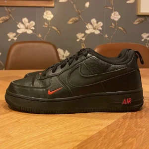 Nike Air Force 1 Limited Edition – Svarta med röd text (strl 37) - Säljer ett par Nike Air Force 1 Limited Edition i svart med röd text – riktigt snygga och unika! Storlek 37. Skorna är i fint skick. Lite använda men känns som nya. Perfekta för dig som vill ha en stilren men ändå speciell look