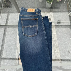 👖 Nudie Jeans Co – Slim fit W32 L32 - Snygga och klassiska Nudie Jeans i mörkblå denim med den ikoniska vita sömmen på bakfickorna. Passformen är slim fit med normal midja – sitter perfekt utan att bli för tighta.  ✨ Detaljer: 	•	Storlek: W32 L32 	•	Färg: Mörkblå / Indigo 	•	Material: 100% ekologisk bomull 	•	Skick: Mycket bra, inga hål eller fläckar 	•	Läderpatch med Nudie-logo bak 	•	Tillverkade i högkvalitativ denim som formar sig snyggt efter kroppen  🧵 Klassiska, hållbara jeans som funkar till allt –ifrån svenska nudie jeans co