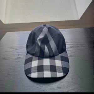 Svartvit  keps  Burberry - Snygg keps från Burberry i svart och vitt med klassiskt rutigt mönster på skärmen och panelerna. Kepsen har böjd skärm och justerbar passform. Perfekt accessoar för att lyfta din streetwear-look.