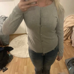 Grå kofta med knappar - Snygg grå kofta med rund hals och knappar framtill. Modellen är långärmad och har en enkel, klassisk design som passar till jeans eller kjol. Materialet känns mjukt och bekvämt mot huden, perfekt för lager-på-lager under kyliga dagar.