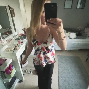 Blommig linnetopp med öppen rygg - Säljer en söt linnetopp med blommigt mönster i rosa, blått och rött på vit botten. Toppen har smala axelband som korsas och knyts i ryggen, vilket ger en snygg öppen rygg. Perfekt för varma dagar och sommarhäng!